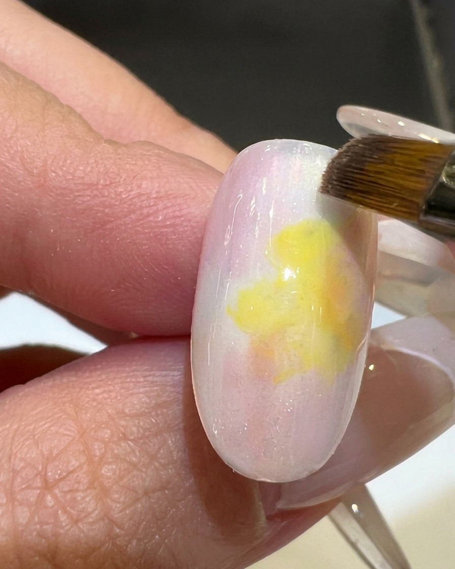 Ein Flachpinsel glättet den Farbverlauf zwischen Rosa und Gelb auf einem Nageltip.