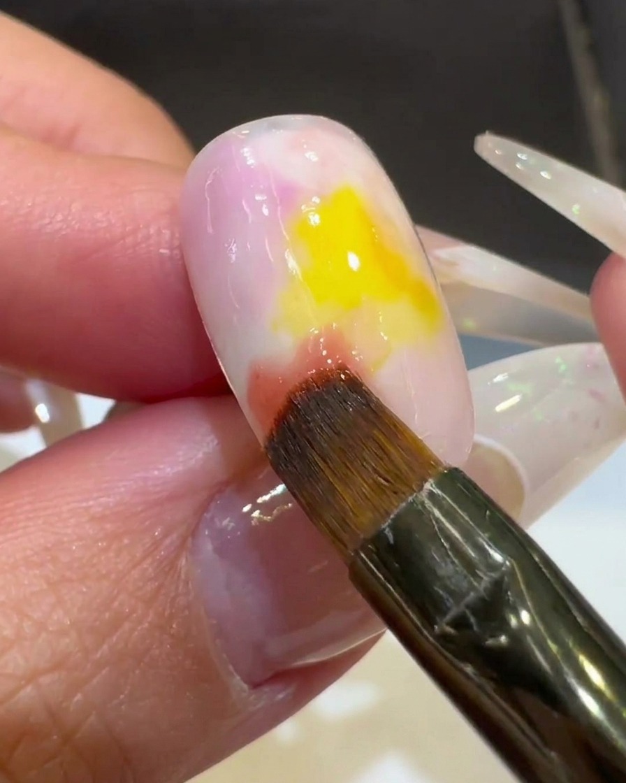 Nahaufnahme eines Nagelpinsels, der rosa Gel in das gelbe Zentrum verblendet, um einen Ombré-Look zu kreieren.