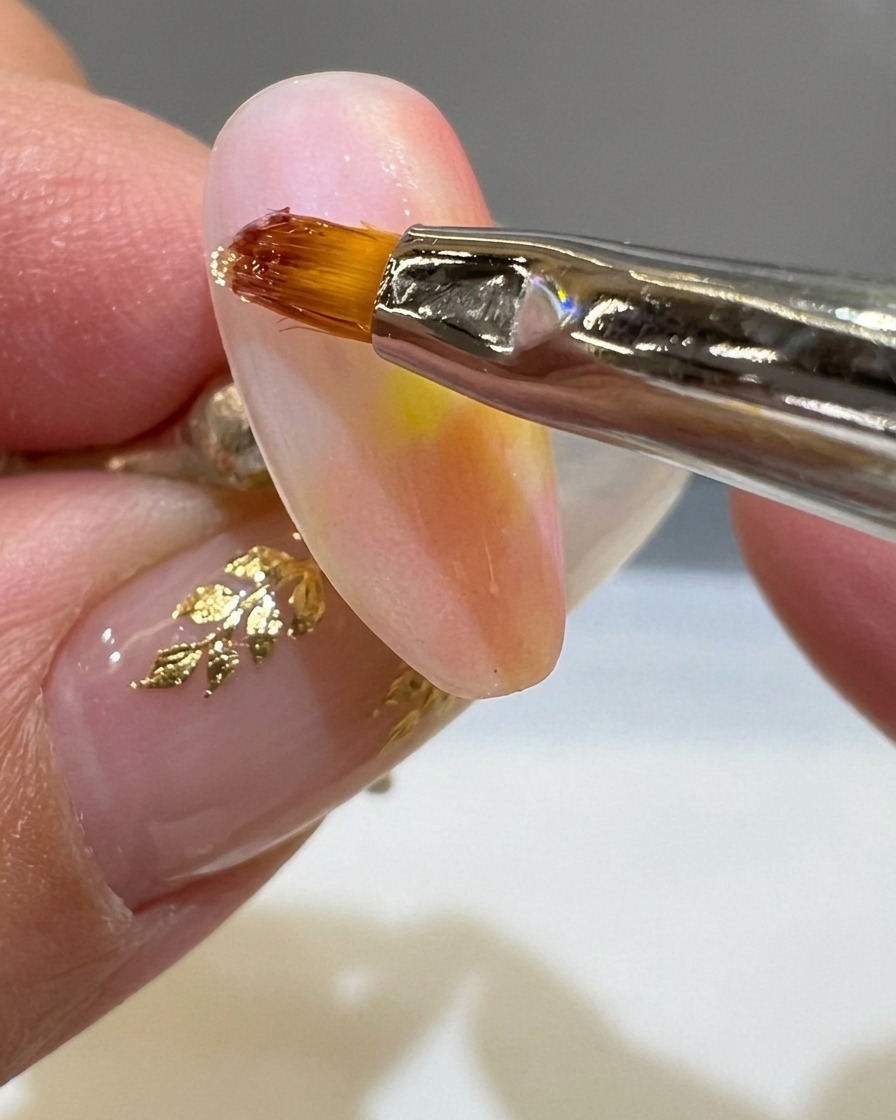 Ein feiner Liner-Pinsel zieht eine dicke Linie aus klarem 3D-Gel auf einen matten Nagel im Sonnenuntergangs-Look.