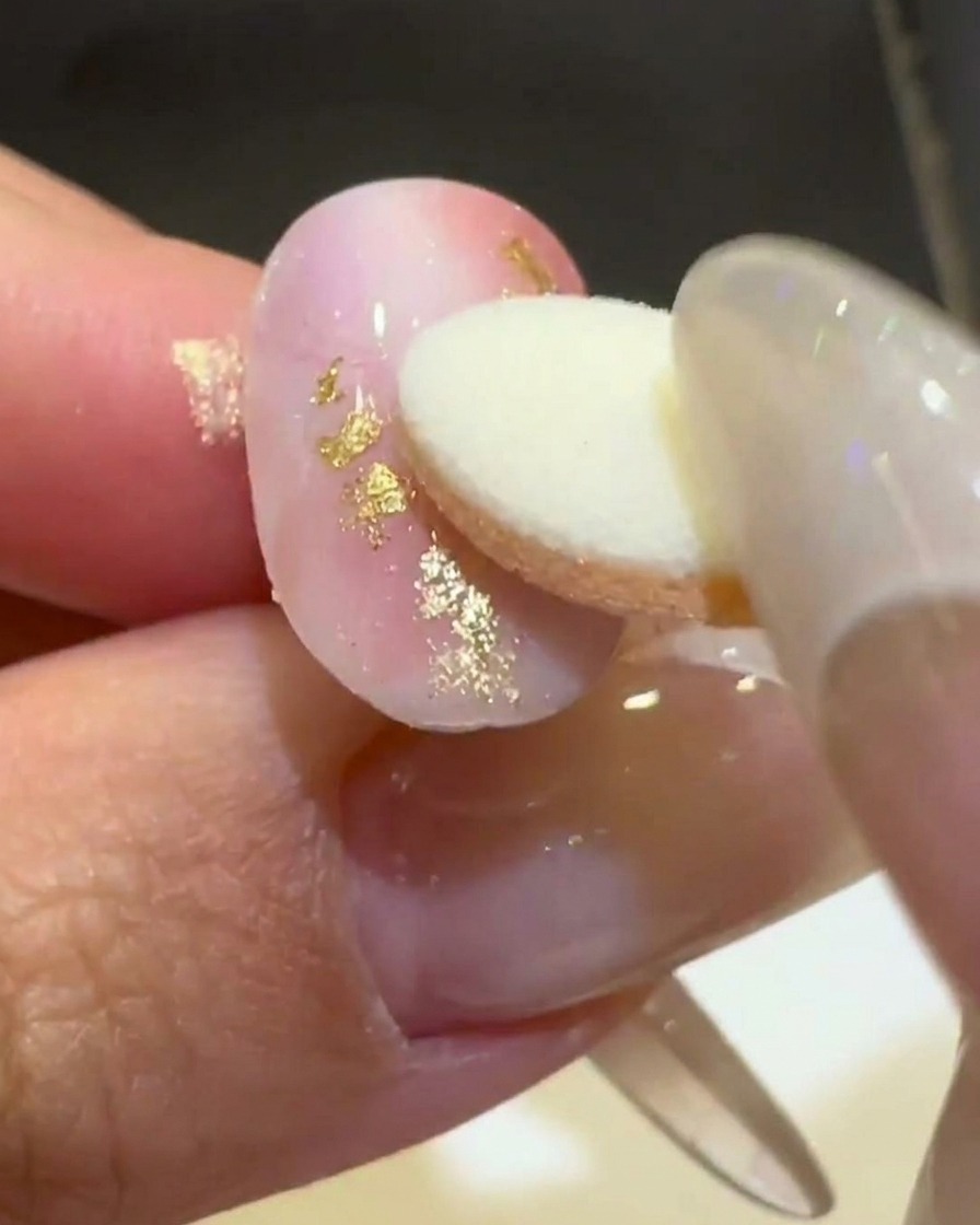 Ein Schwamm-Applikator reibt goldenes Aurora-Chrompuder auf eine erhabene 3D-Welle auf einem matten, rosa-weißen Nagel.