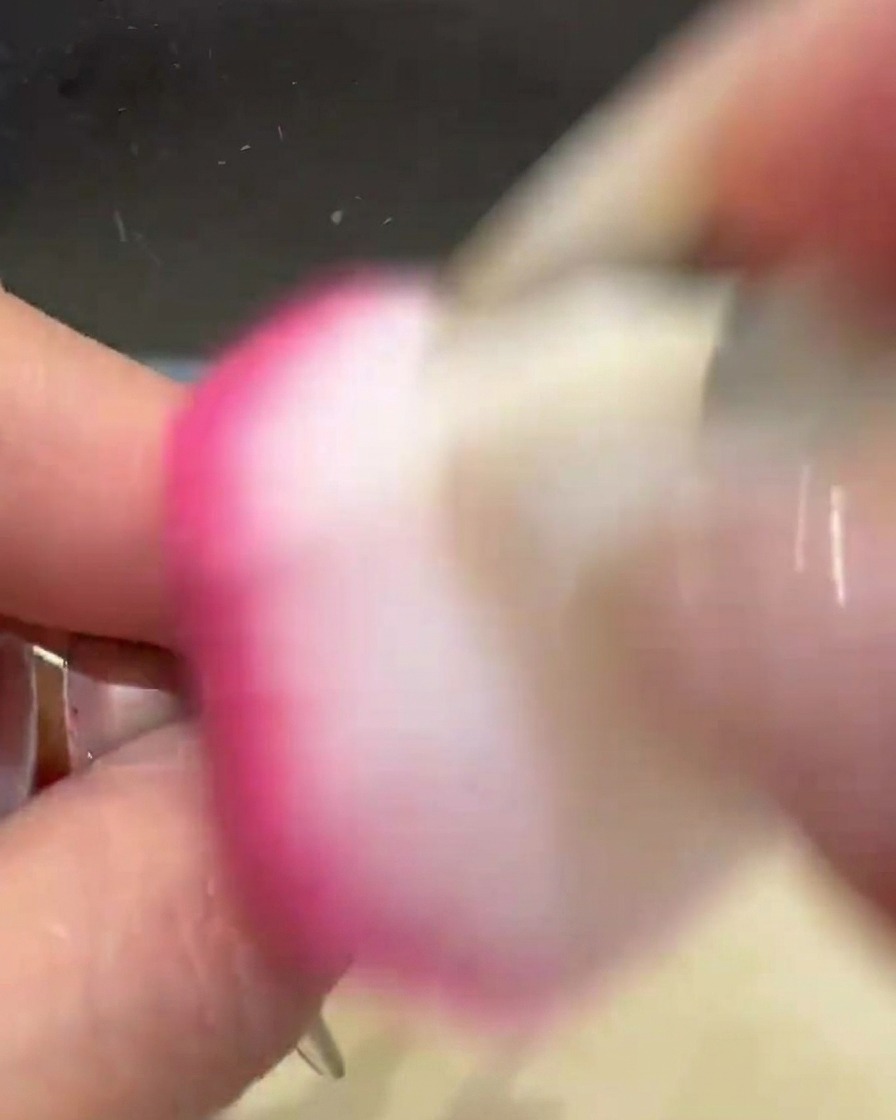 Ein rosa Staubpinsel fegt über den Nagel, um überschüssiges goldenes Chrompuder zu entfernen.