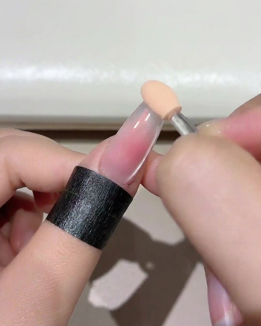 Nahaufnahme eines Schwämmchens, das ein sanftes Blush-Rosa-Gel auf die Nagelspitze auftupft.