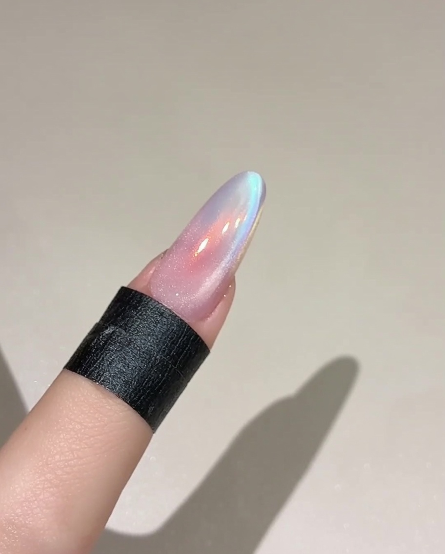Ein Pinsel trägt eine Schicht schimmerndes, transparentes Cat-Eye-Gel auf einen bereits farbigen Nagel auf.