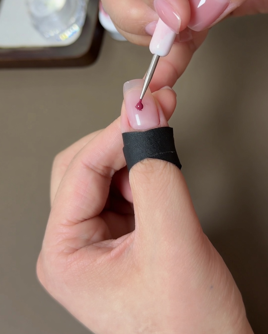 Ein kleines Werkzeug setzt einen Punkt pfirsichfarbenes Gel in die Mitte eines nudefarbenen Nagels.