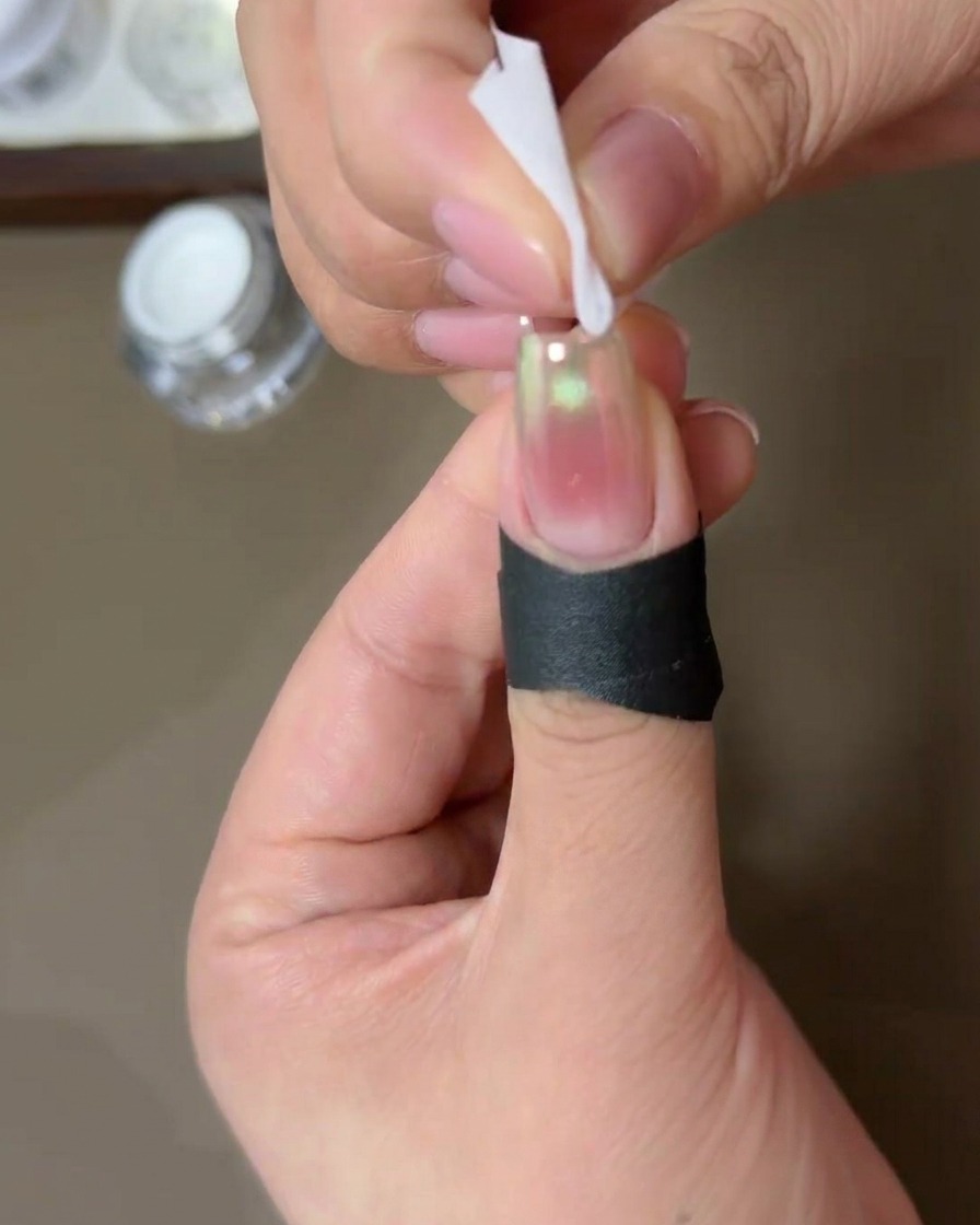Die Kanten eines mit Chrom-Puder bestäubten Nagels werden mit einem in Alkohol getränkten Tuch gereinigt.