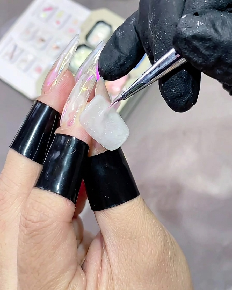 Ein dünner Liner-Pinsel trägt einen Streifen aus rosa Hochglanz-Strukturgel horizontal auf einen weiß lackierten Nagel auf.