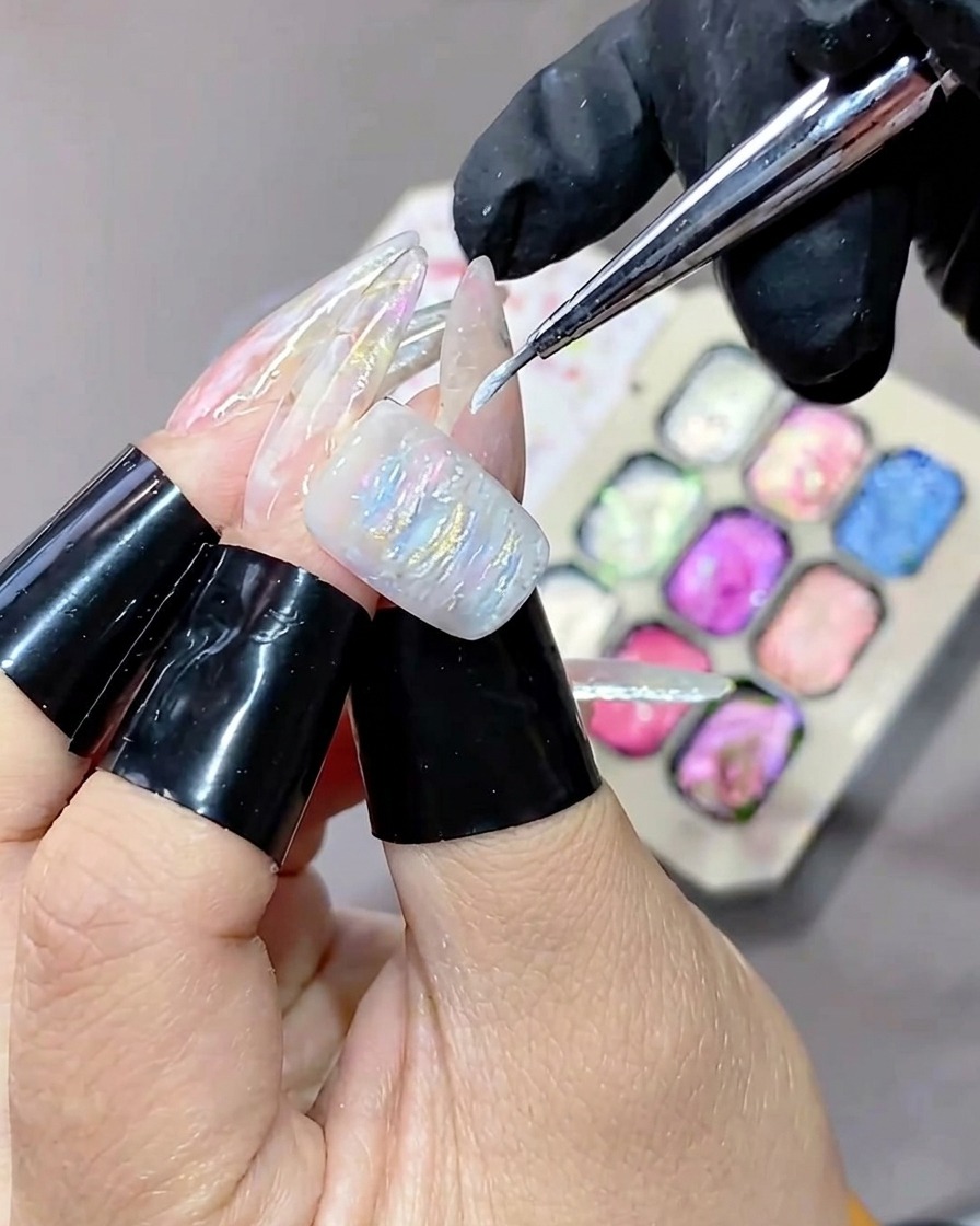 Ein Pinsel mit feiner Spitze trägt weißes Highlight-Gel auf die strukturierte Oberfläche einer Gelmaniküre auf.