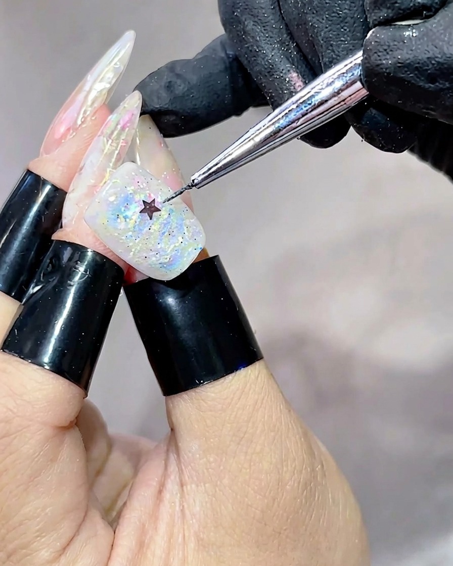Ein Metallwerkzeug platziert eine kleine, schwarze sternförmige Paillette in der Mitte eines mit schillerndem, mehrfarbigem Gel bedeckten Nagels.