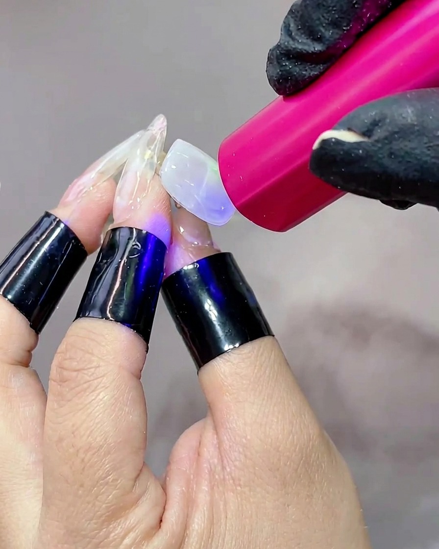 Eine Hand unter einer tragbaren UV-Lampe, wobei die Nageloberfläche leuchtet, während das Gel aushärtet.