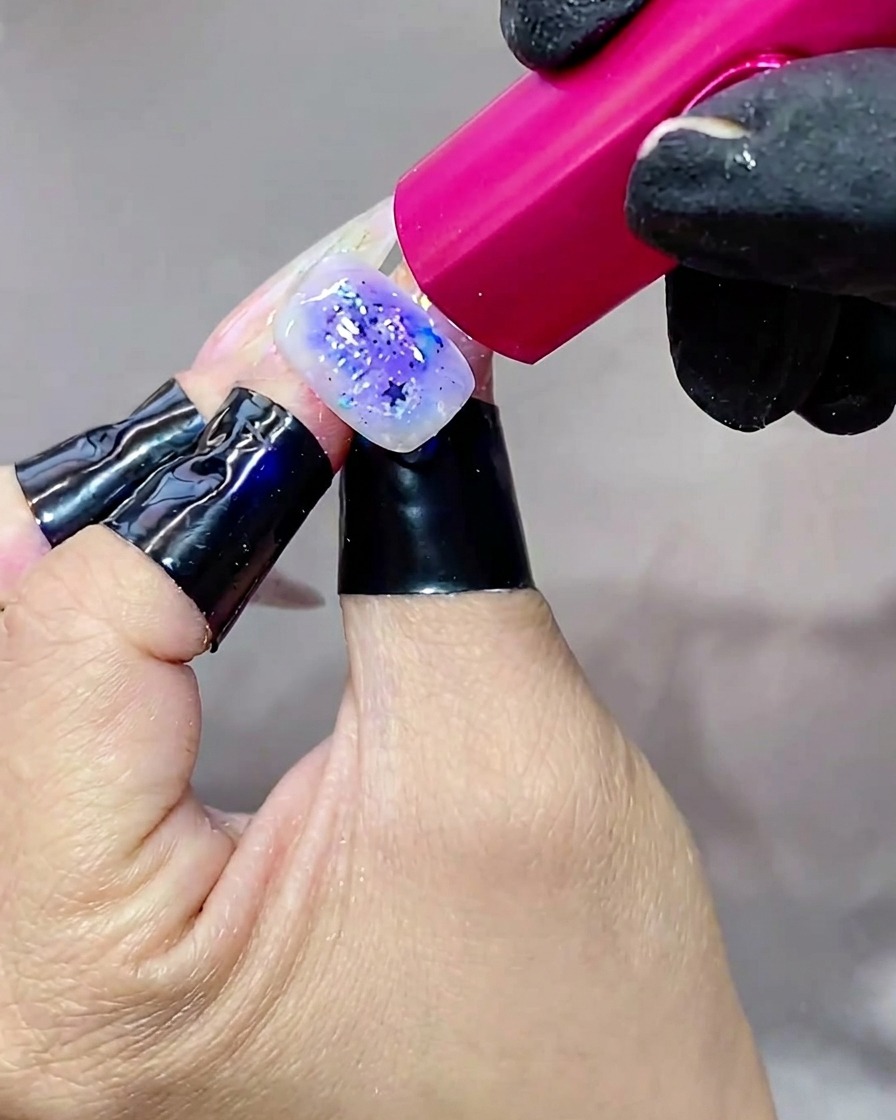 Eine Hand hält einen Nagel unter eine helle UV-Lampe und härtet die letzte Top-Coat-Schicht aus.