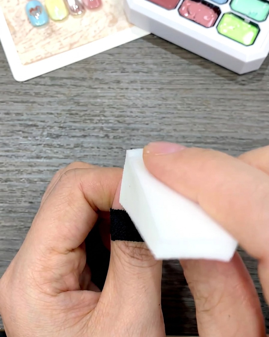 Eine Hand nutzt ein weißes Kosmetikschwämmchen, um das gelbe Gel sanft nach unten auf den Nagel zu tupfen.
