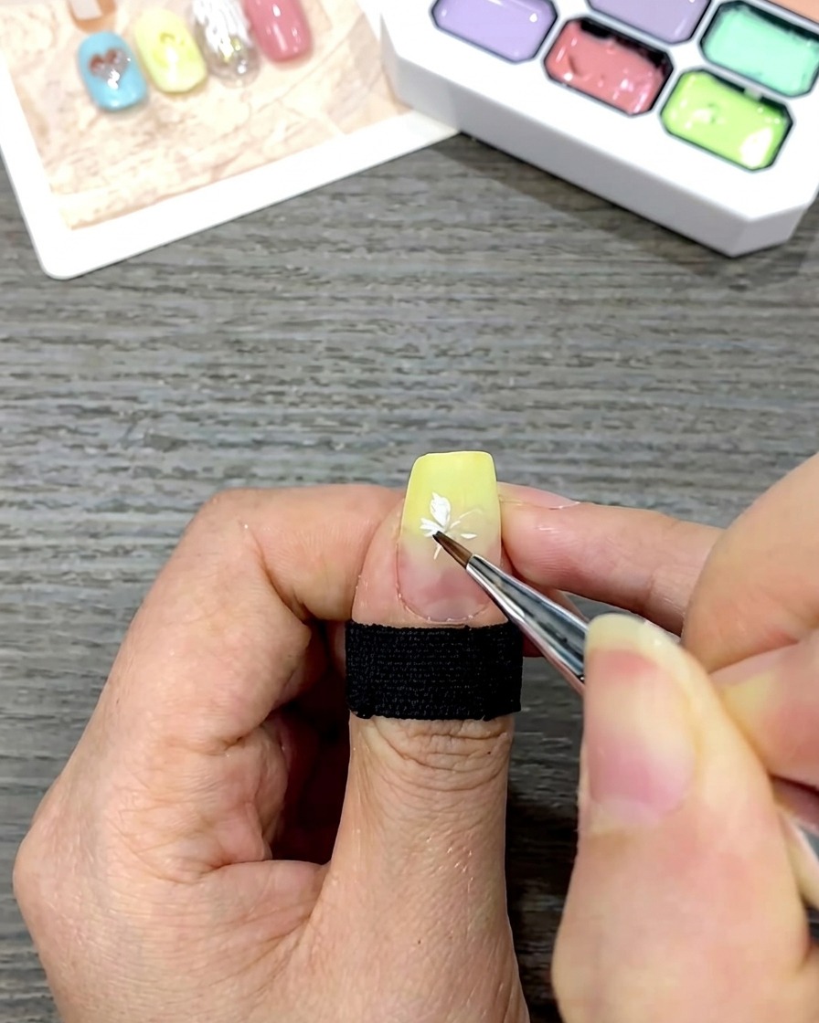 Nahaufnahme eines Nagels mit einer fertig gemalten weißen Gänseblümchen-Blüte auf dem gelben Verlauf.