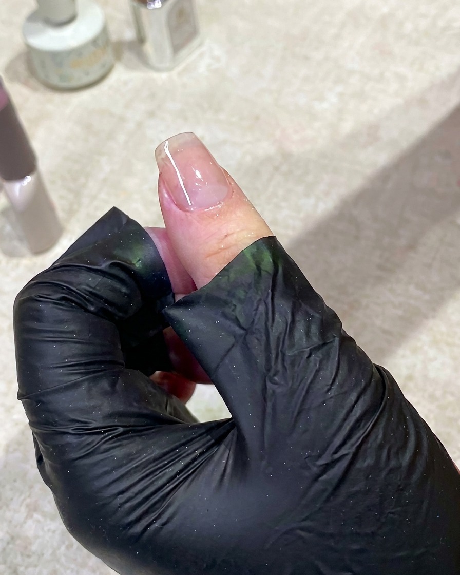 Eine Hand liegt in einer eingeschalteten UV-Nagellampe, um den Base Coat auszuhärten.