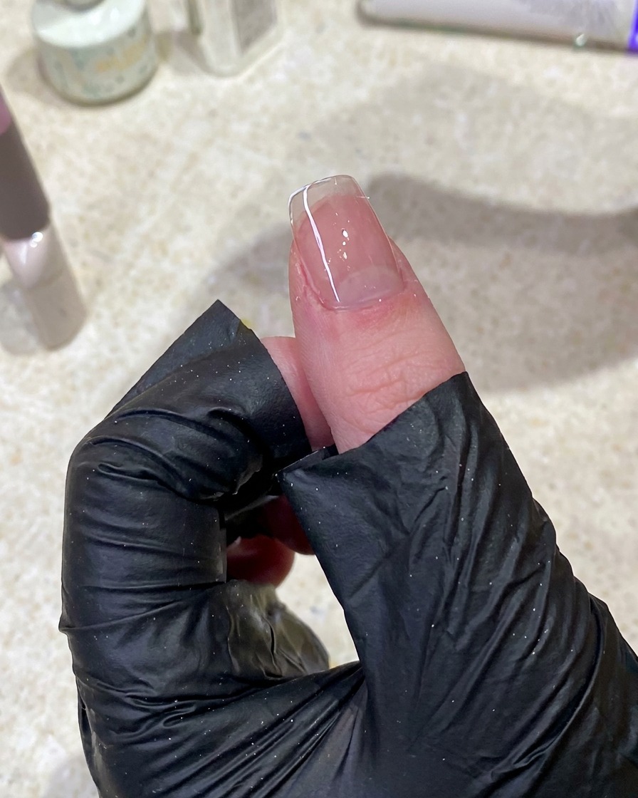 Nahaufnahme einer Hand, die mit einem fusselfreien Pad die Oberfläche eines manikürten Nagels reinigt.