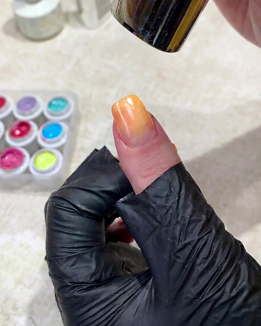 Eine Hand wird unter eine UV-Lampe gelegt, um das frisch aufgetragene Ombré-Gel auszuhärten.