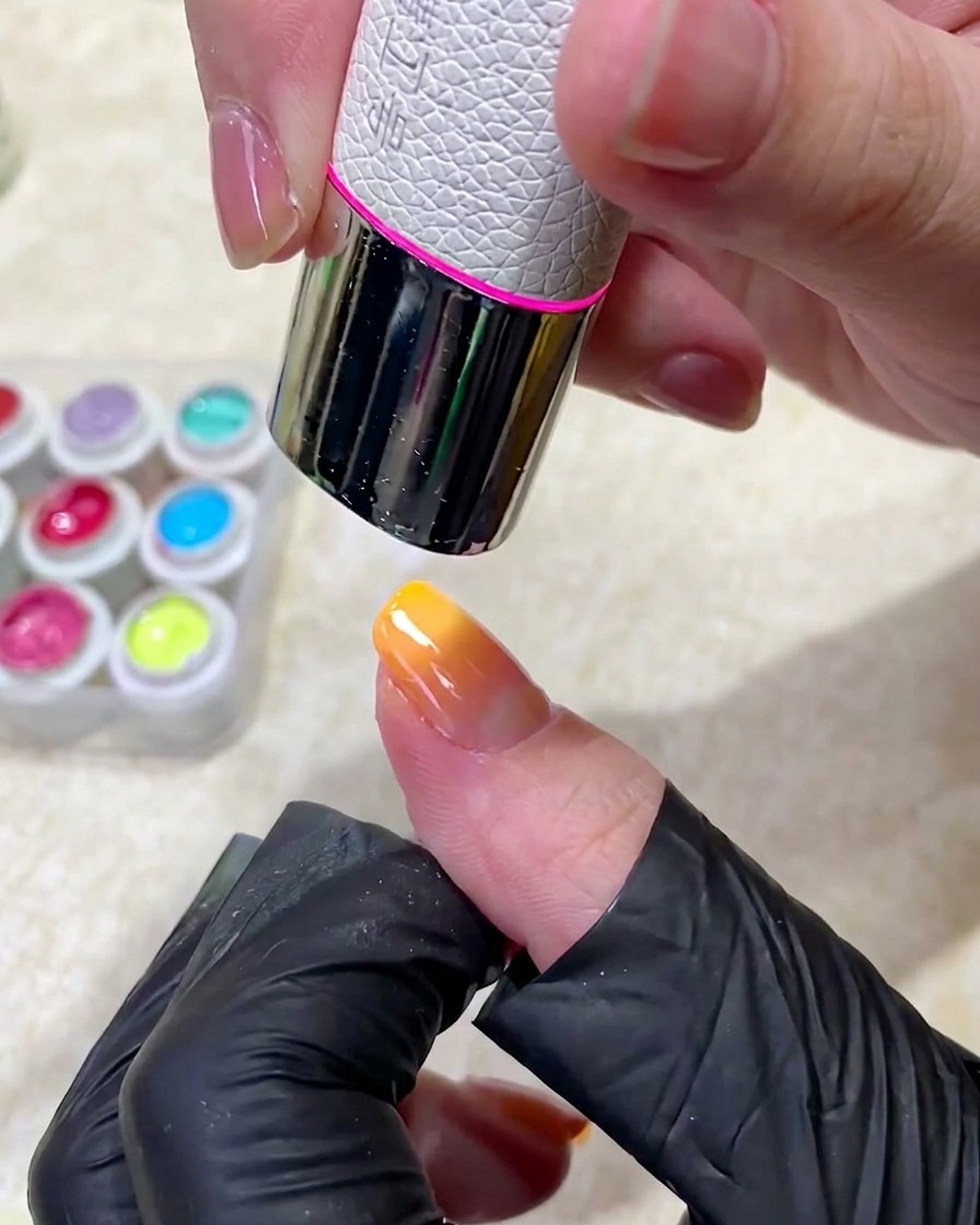 Ein manikürter Finger wird unter eine professionelle UV-Lampe gelegt, um die Gelschichten auszuhärten.