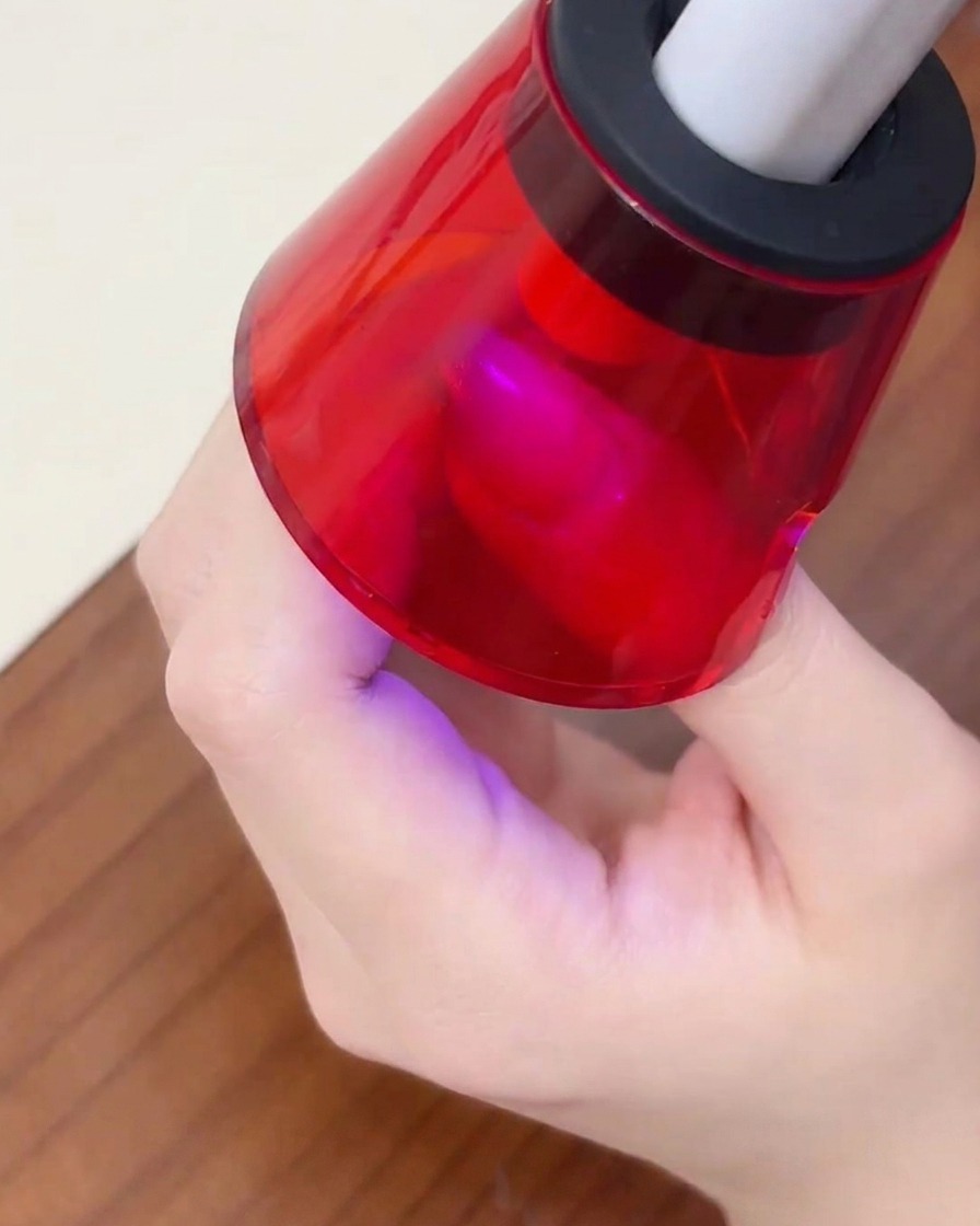 Ein Finger liegt unter einer roten, tragbaren Mini-UV-Lampe, um das Farbgel auszuhärten.