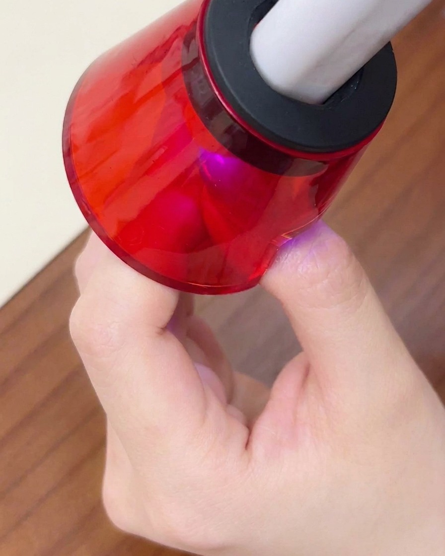 Nahaufnahme eines Fingers unter einer roten UV/LED-Minilampe für die letzte Aushärtung.