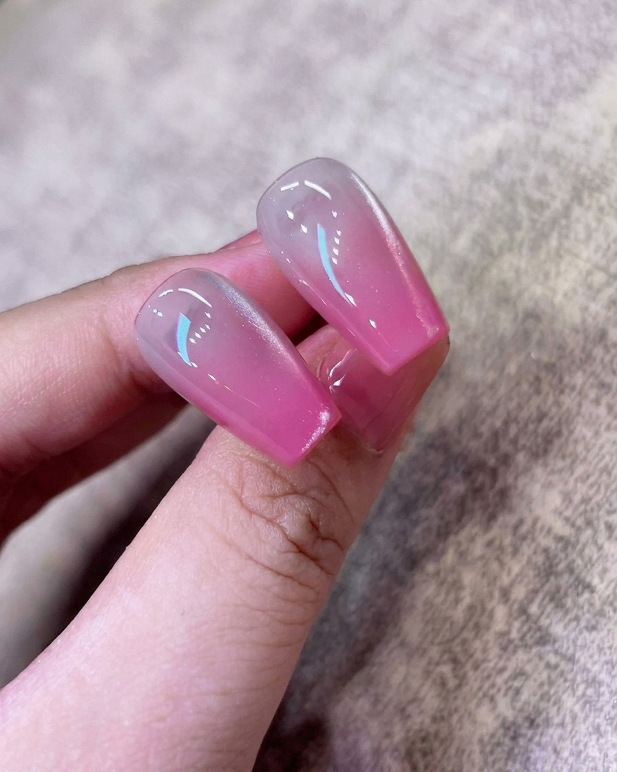 Ein Pinsel trägt eine Schicht des schimmernden, weißen Cat-Eye-Gellacks über den pinken Ombré-Nagel auf.