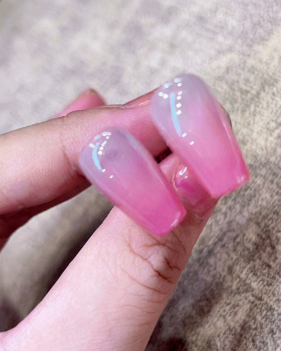 Nahaufnahme eines Pinsels, der einen klaren, hochglänzenden Top Coat über einen pinken Ombré-Nagel streicht.