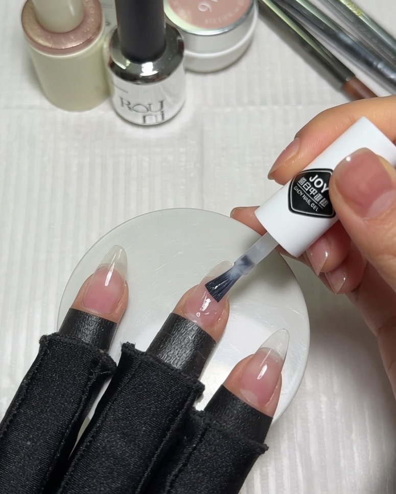 Auftragen von milchig weißem Gel-Nagellack auf die obere Hälfte eines vorbereiteten rosafarbenen Nude-Nagels mit dem Pinsel des Fläschchens.