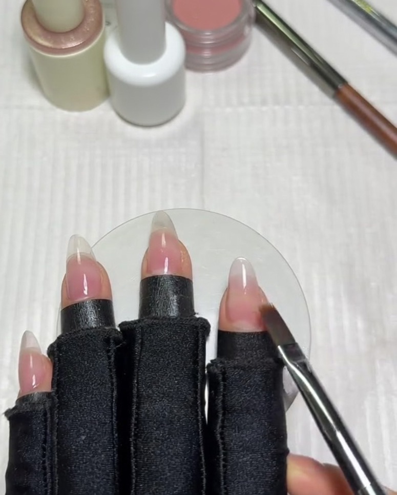Ein flacher Ombré-Pinsel wischt horizontal über den Nagel, um die Kante des milchig weißen Gel-Lacks in die Nude-Basis zu verblenden.