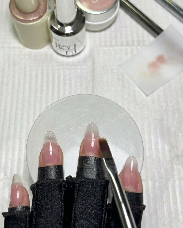 Ein sauberer, flacher Ombré-Pinsel, der sanft die Kante des milchig weißen Gels auf einem benachbarten Fingernagel verblendet.
