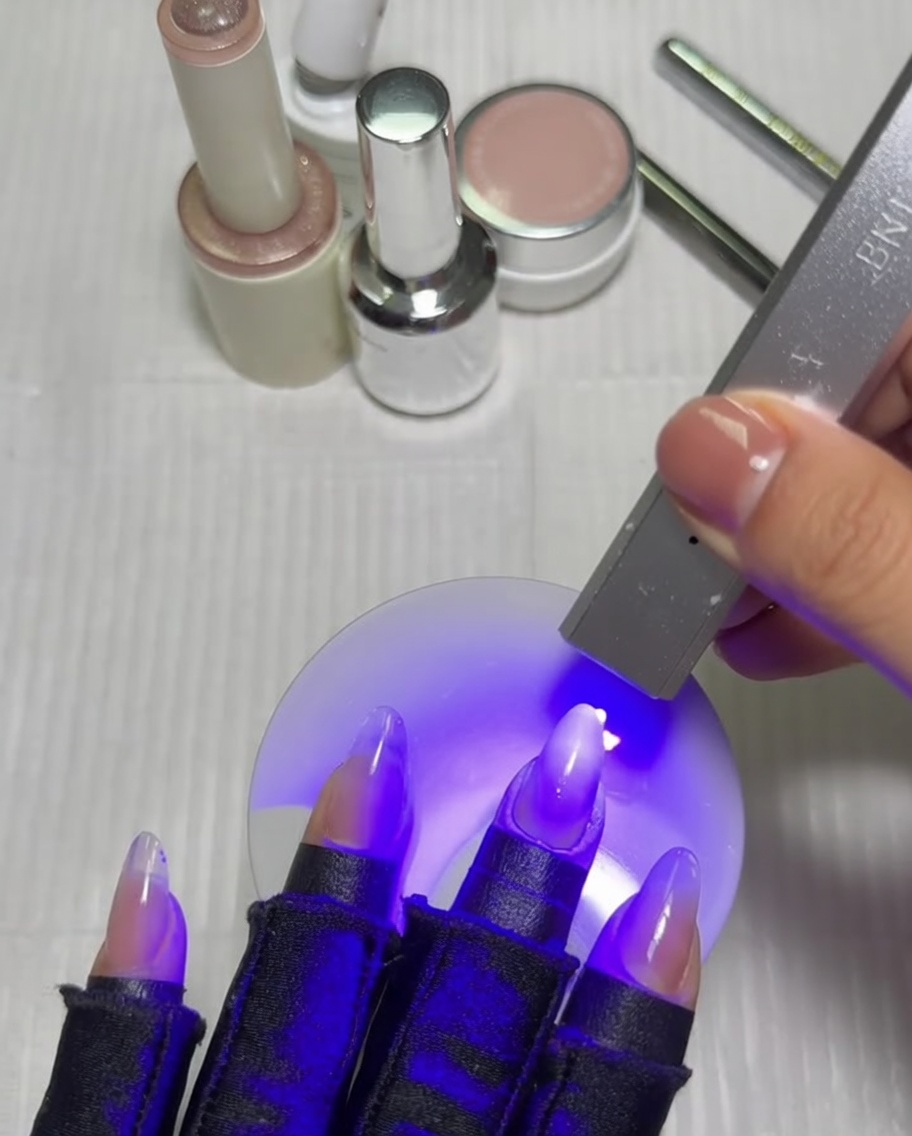 Eine Hand mit einer Ombré-Maniküre in einer UV/LED-Lampe, die unter violettem Licht aushärtet.