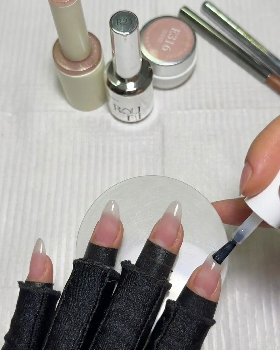 Ein Nagelpinsel trägt eine kleine Menge milchig weißes Gel auf die Nagelspitze auf.