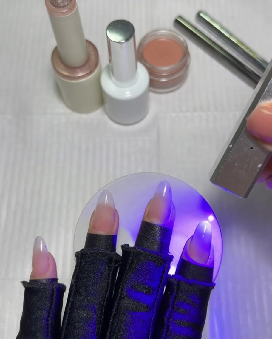 Ein flacher Ombré-Pinsel verblendet eine weiße Gelschicht auf einem Fingernagel.