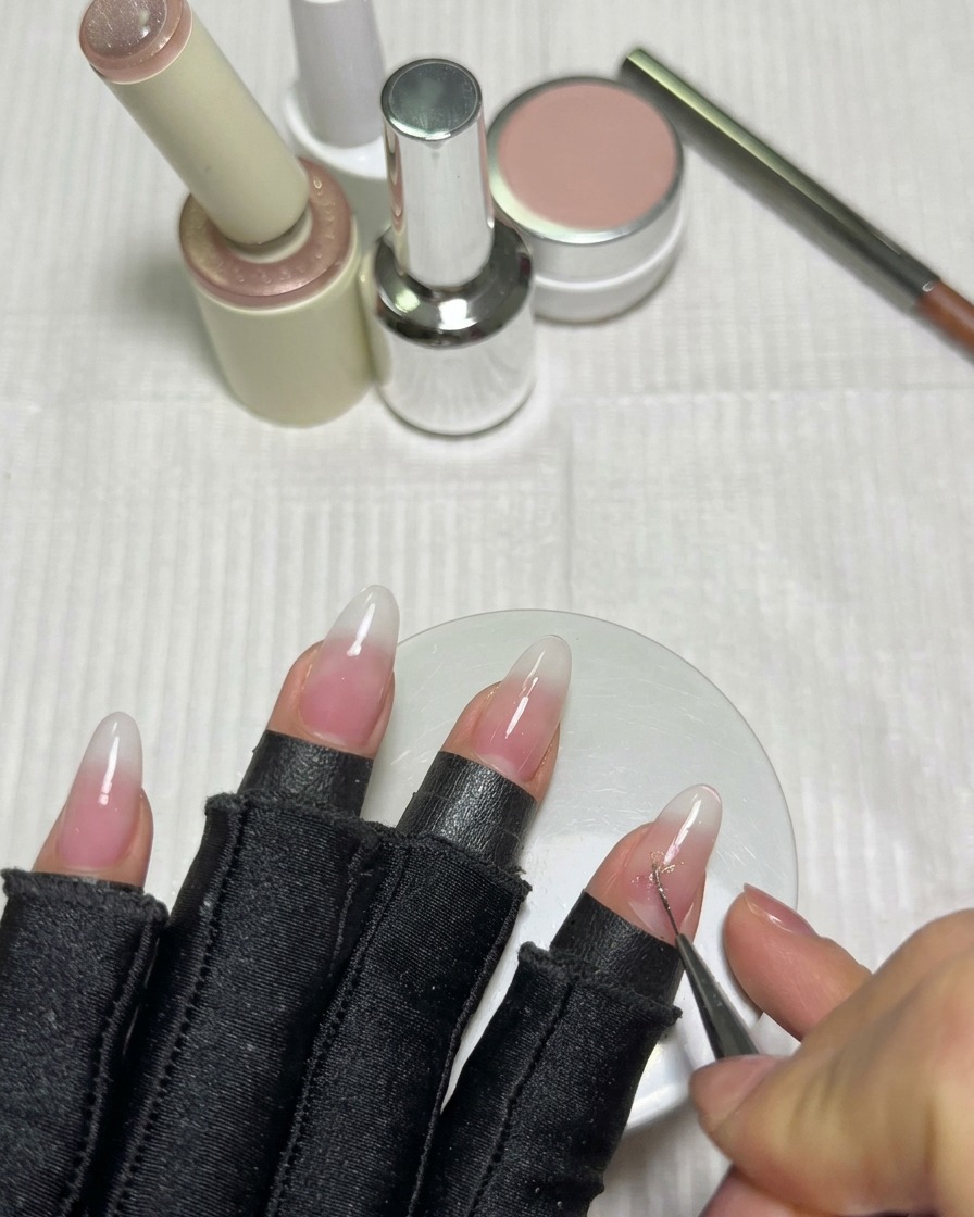 Ein feiner Liner-Pinsel zeichnet die sich kreuzenden Linien eines Sterns mit rosa Cat-Eye-Gel auf einem milchig weißen Nagel.