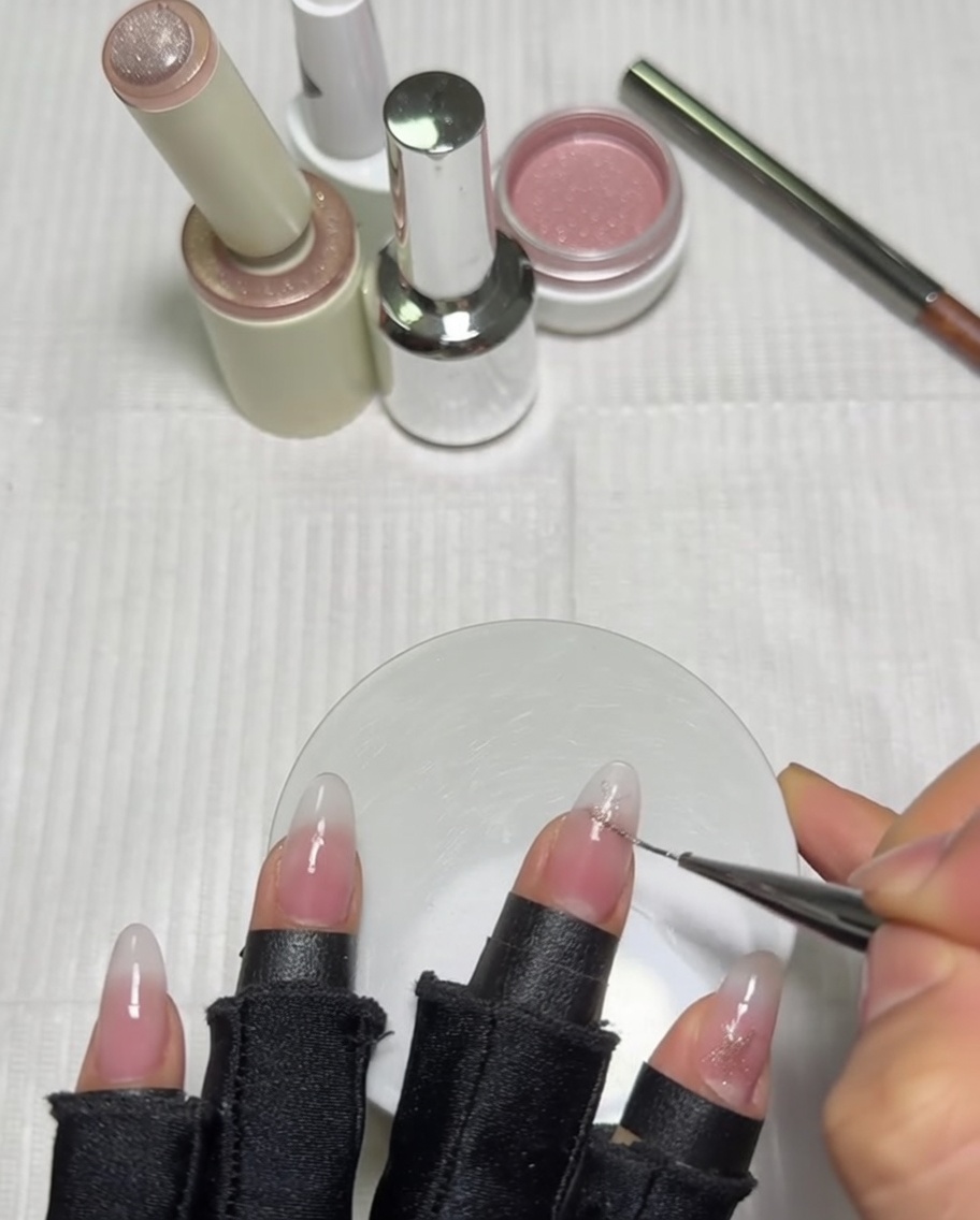 Nahaufnahme einer Hand, die mit einem langen Liner-Pinsel ein rosa Sterndesign auf einen Daumennagel mit milchiger Ombré-Basis detailliert.