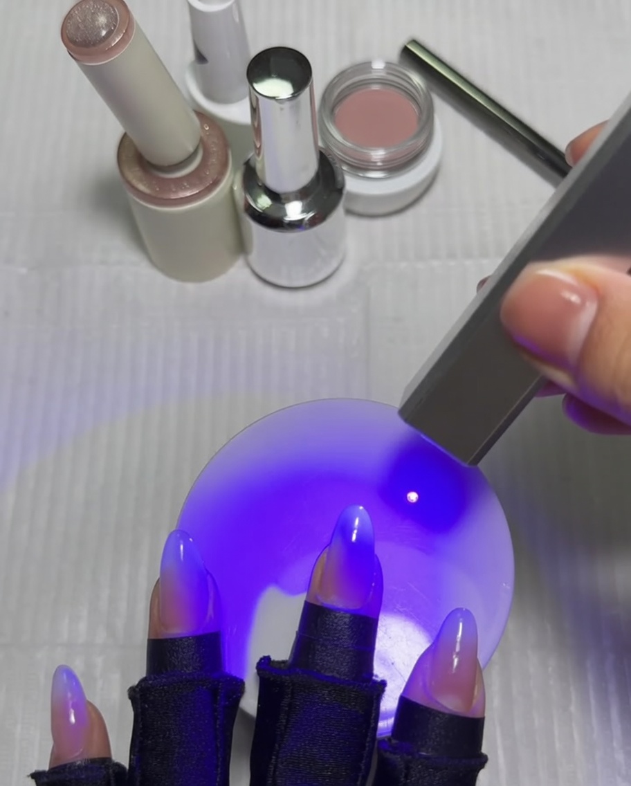 Eine Hand mit Nägeln unter einer UV-Lampe, wobei der Daumen nach Fertigstellung des Cat-Eye-Sterndesigns ausgehärtet wird.