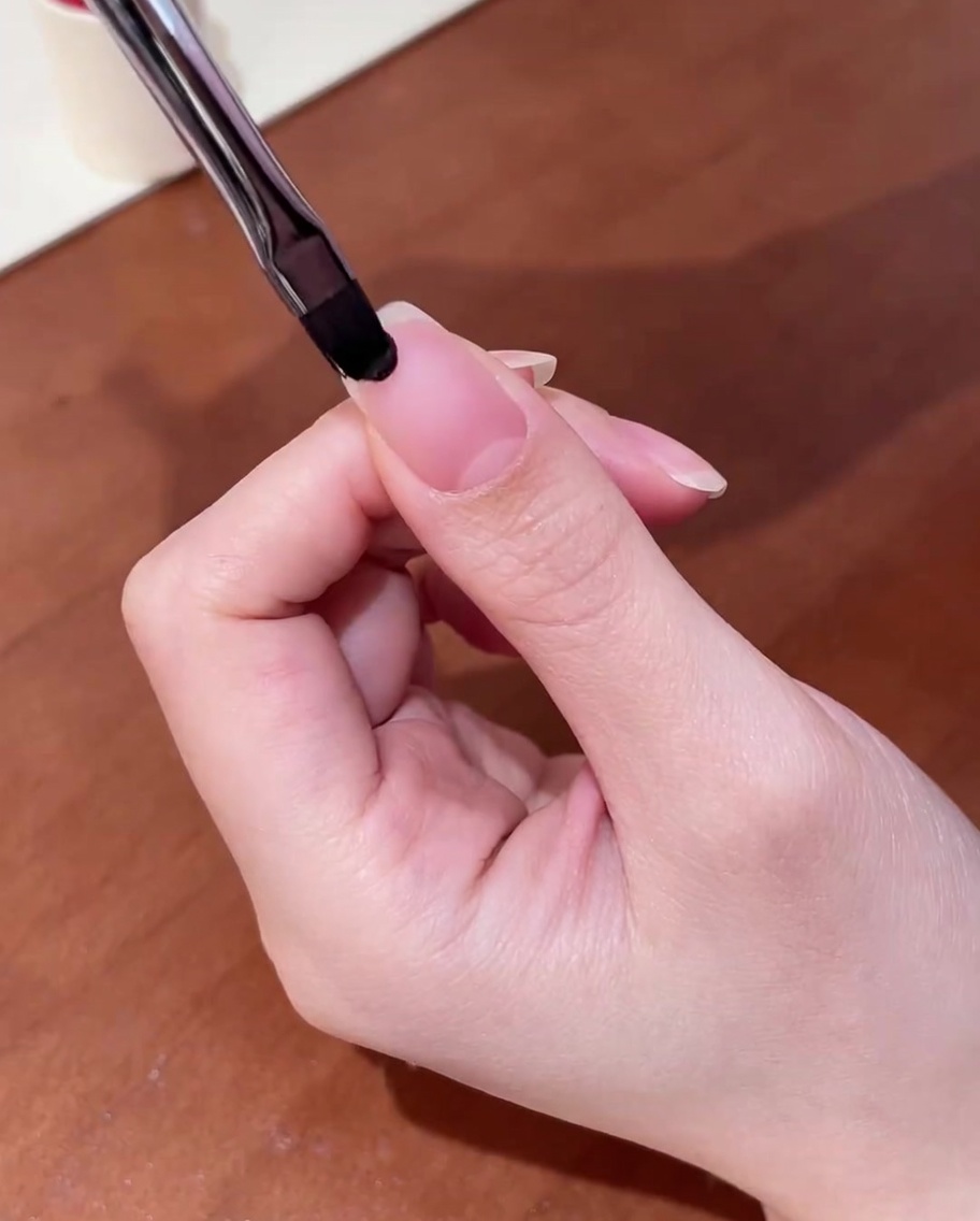 Nahaufnahme eines Pinsels, der klaren Base-Coat auf einen sauberen Naturnagel aufträgt.