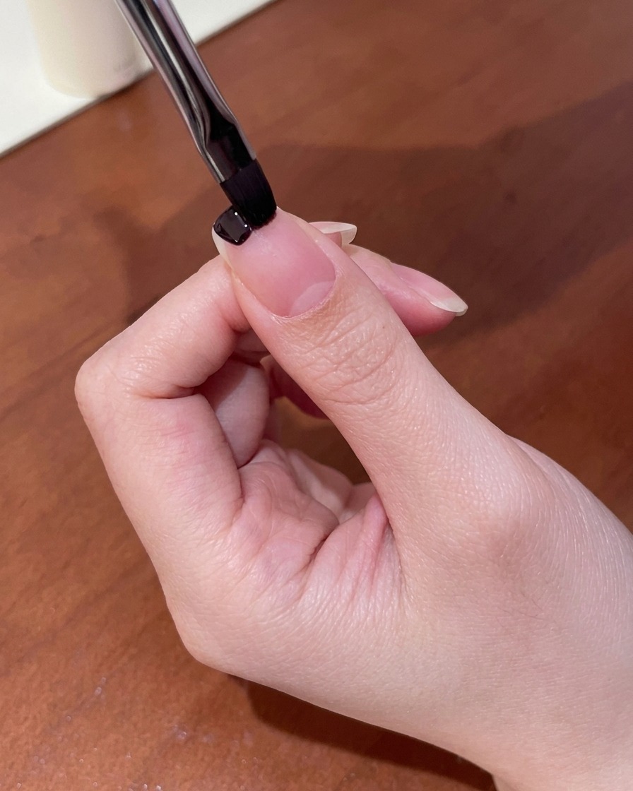 Nahaufnahme eines kleinen Nagelpinsels, der dunkelviolettes Gel an der Nagelspitze aufträgt.