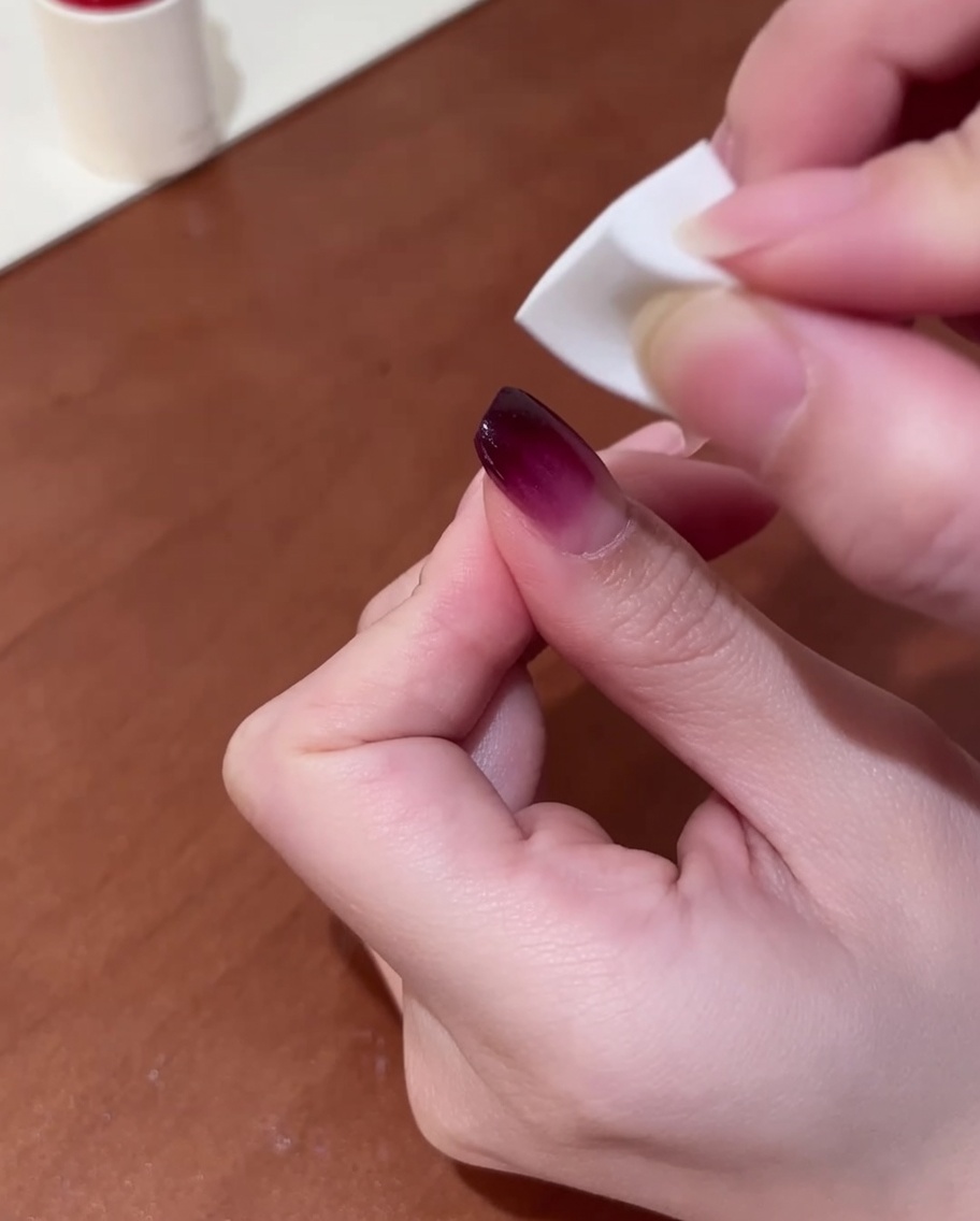 Hand hält ein kleines weißes Make-up-Schwämmchen, das sanft lila Gel auf den Nagel tupft, um einen Verlauf zu erzeugen.