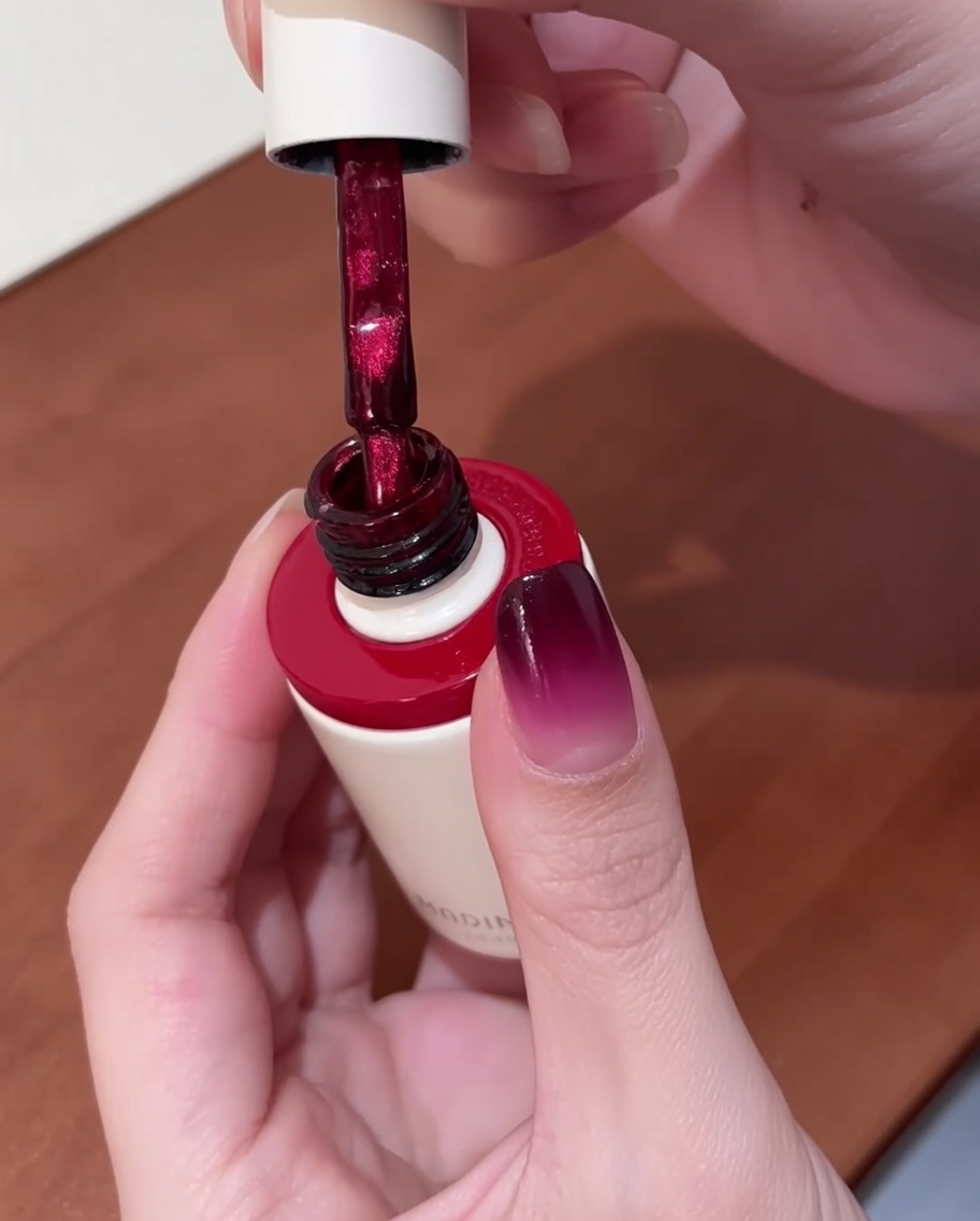 Ein Pinsel trägt leuchtend rotes Cat-Eye-Gel auf einen bereits grundierten Nagel auf.