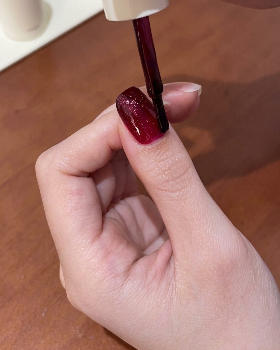 Ein Magnettool wird über einen mit nassem, rotem Cat-Eye-Gel beschichteten Nagel gehalten und zieht den Schimmer in eine helle Linie.