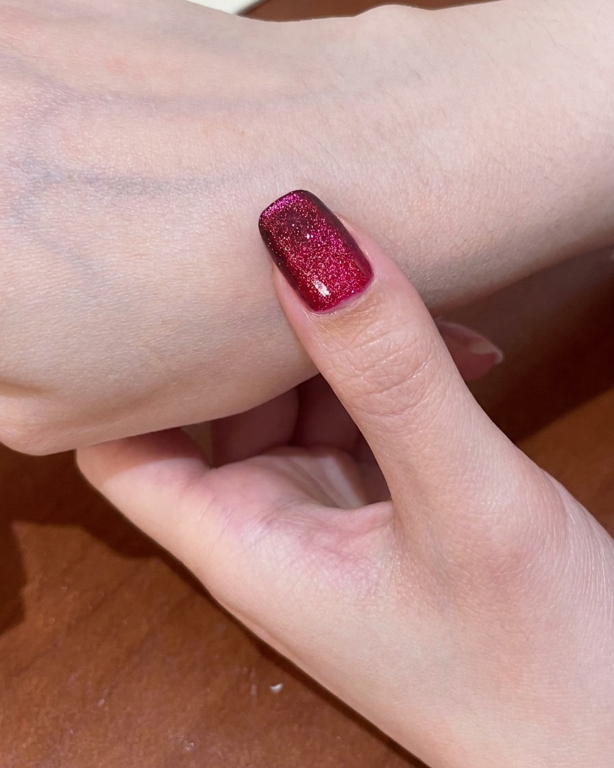 Ein Fingernagel mit dem fertigen roten Cat-Eye-Design wird in einer UV-Lampe ausgehärtet.