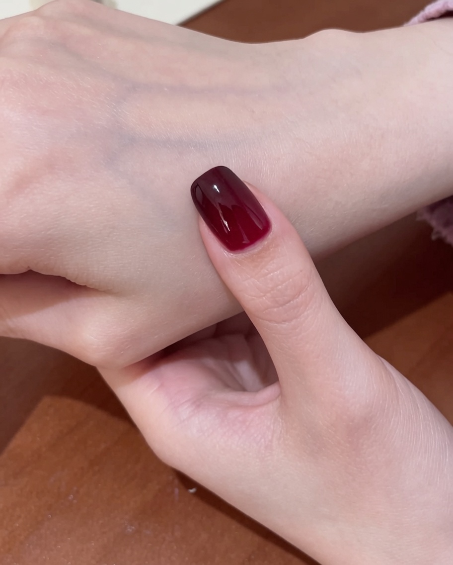 Ein Pinsel trägt klaren, glänzenden Top-Coat über das fertige rote Cat-Eye-Design auf.
