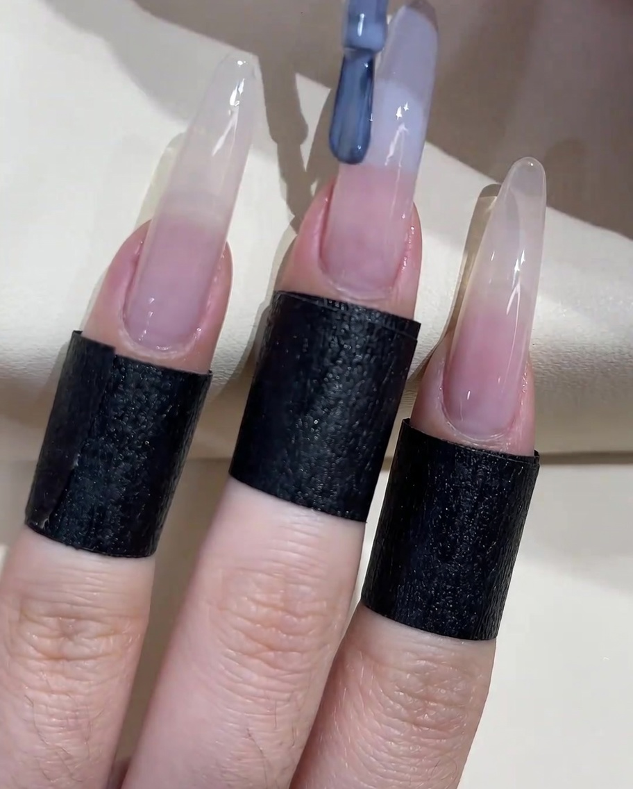 Ein Nagelpinsel trägt graublaues Gel auf die freie Nagelkante auf.