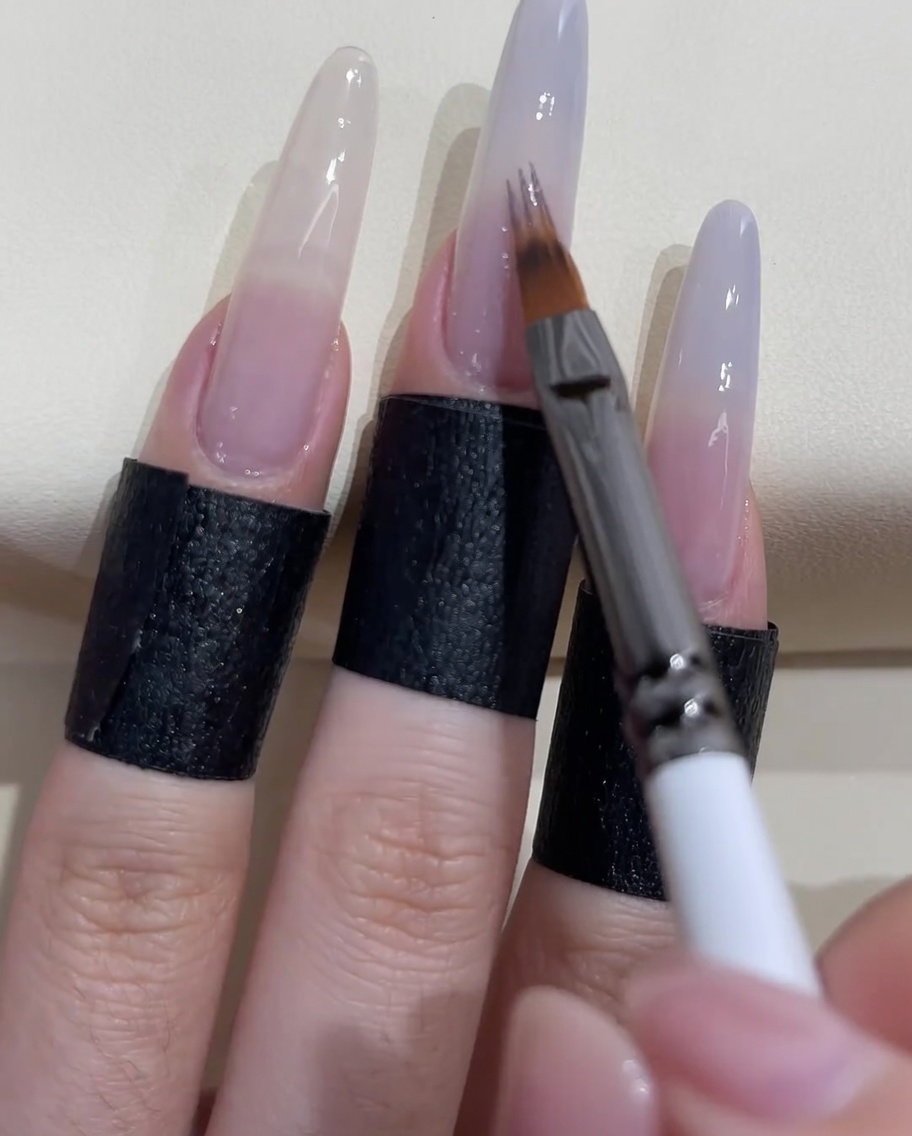 Ein spezieller Ombré-Pinsel verblendet das graublaue Gel nach unten auf dem Nagel.