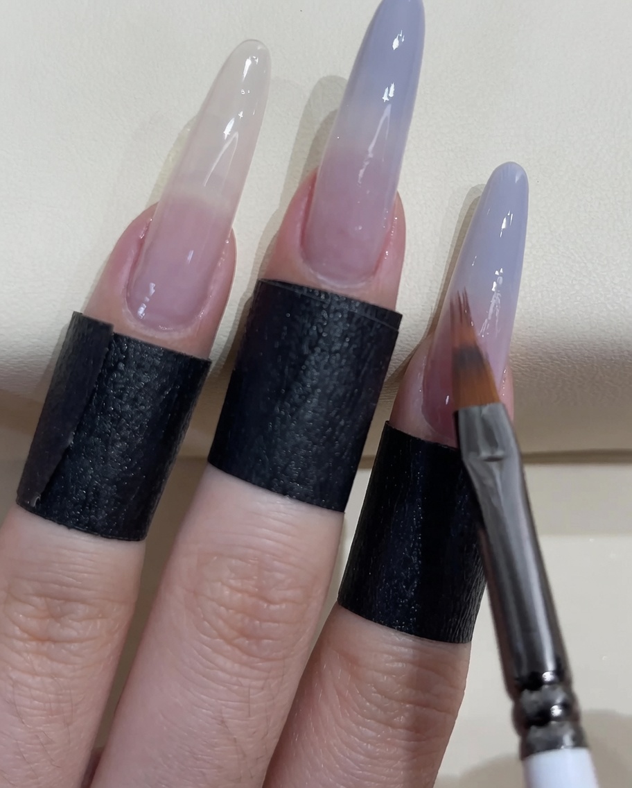 Ein kleiner Nagelpinsel trägt mehr graublaues Gel auf die Nagelspitze auf.