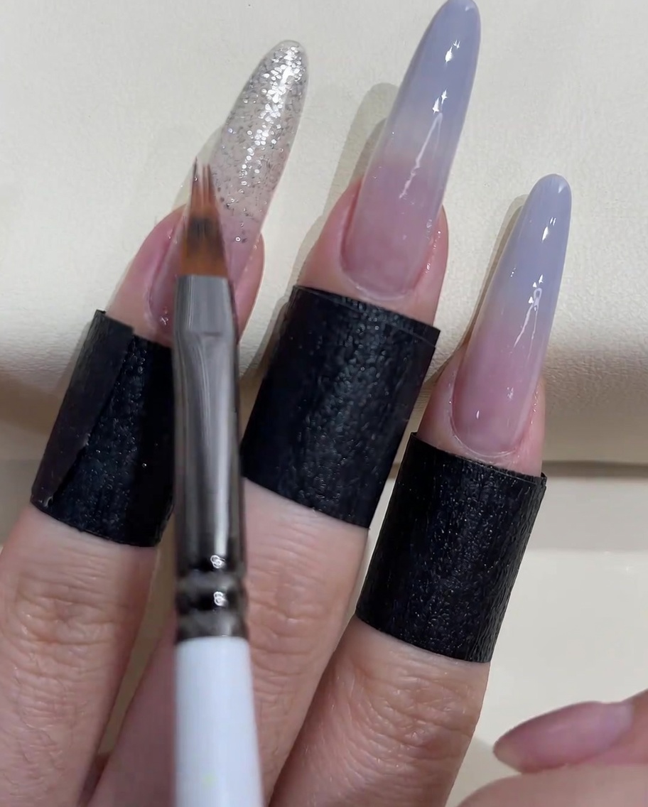 Nahaufnahme eines Pinsels, der den silbernen Glitzer auf der Nagelplatte verblendet.