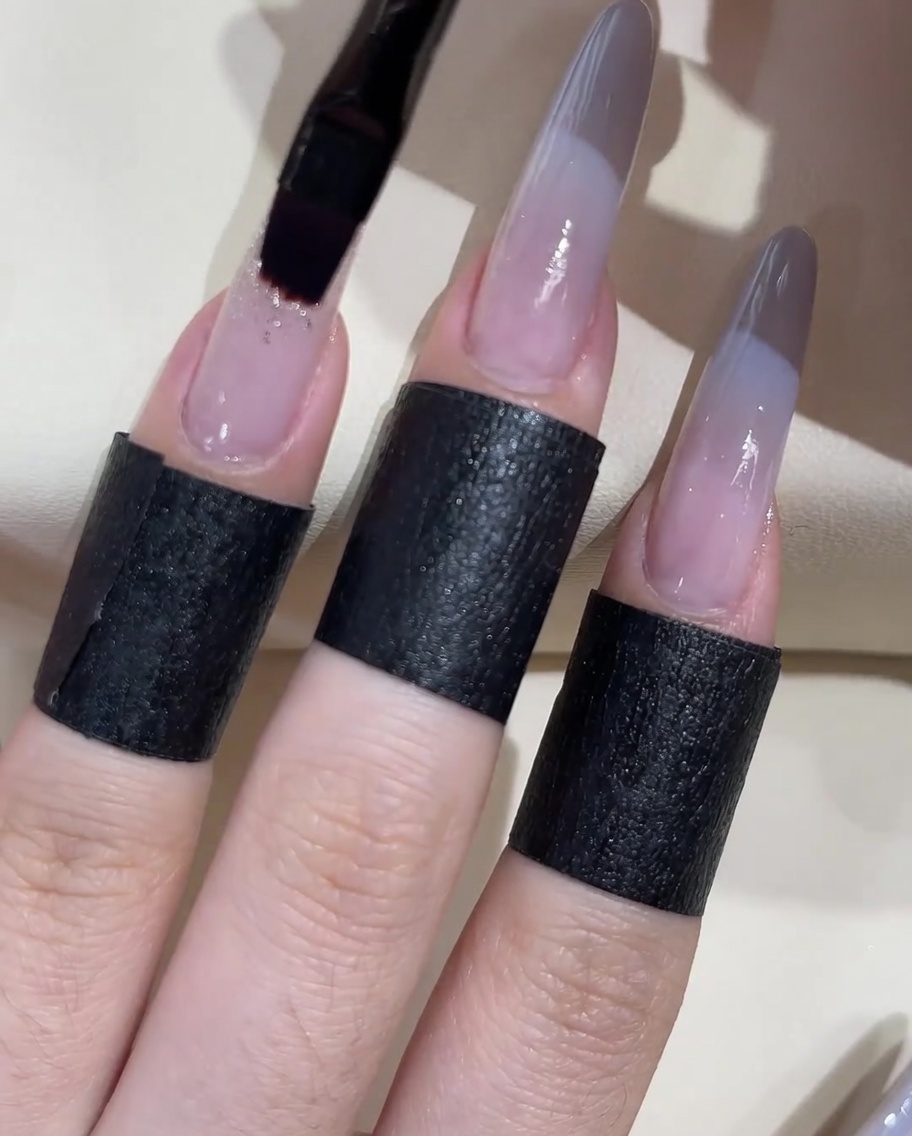 Ein flacher Gelpinsel trägt einen Klecks transparentes Klebegel auf die Nageloberfläche auf.