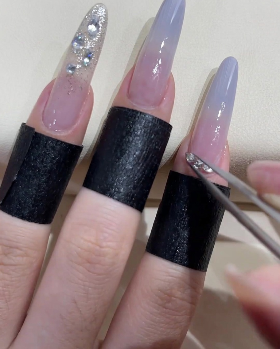 Nahaufnahme einer Pinzette, die kleine Perlen und Steine um die Nagelhaut eines Zeigefingers anordnet.