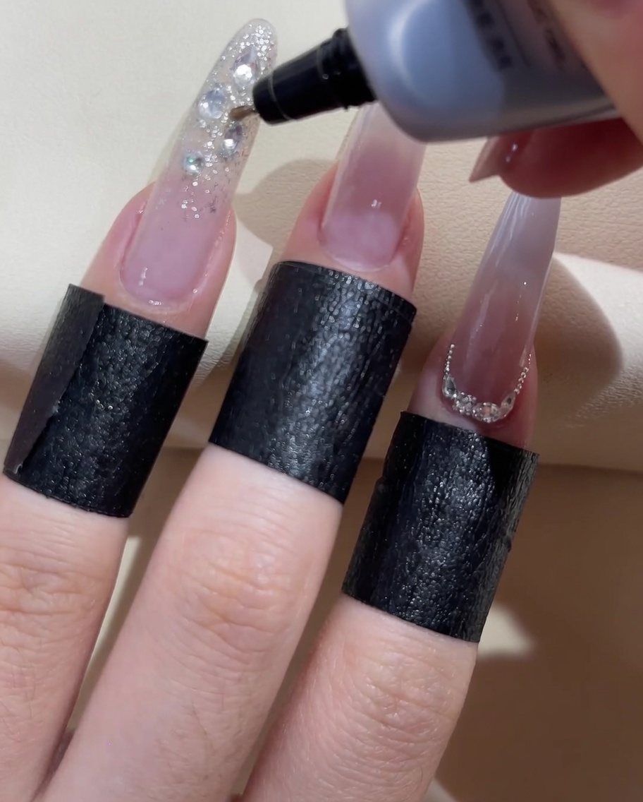 Eine Flasche mit feiner Düse trägt klares Auffüllgel um die Kanten der Nagelsteine auf.
