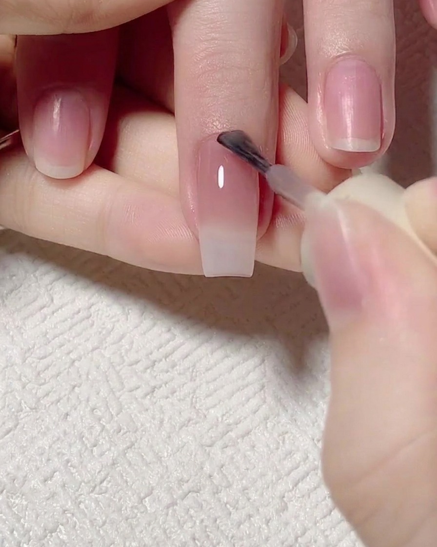 Ein Pinsel trägt ein intensiveres rosa Gel im Bereich der Nagelhaut auf.