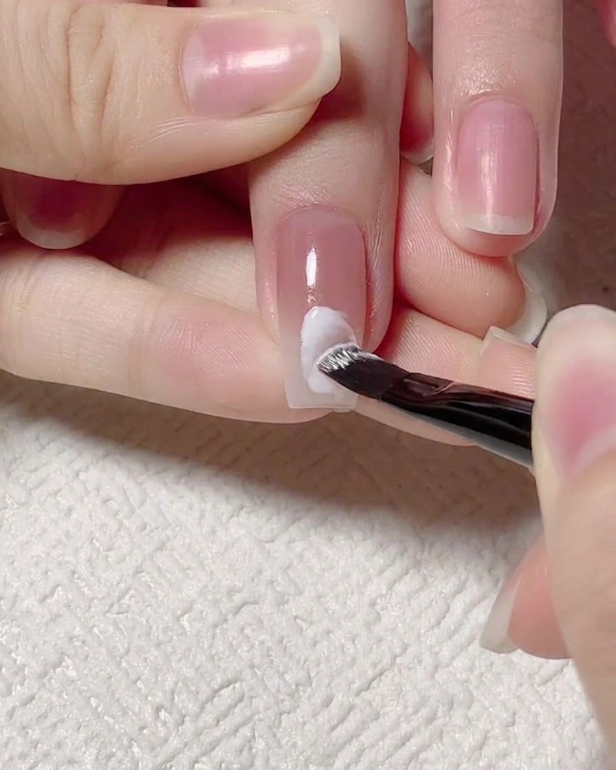 Ein Detailpinsel zeichnet eine weiße Wellenlinie über die Mitte des Nagels.