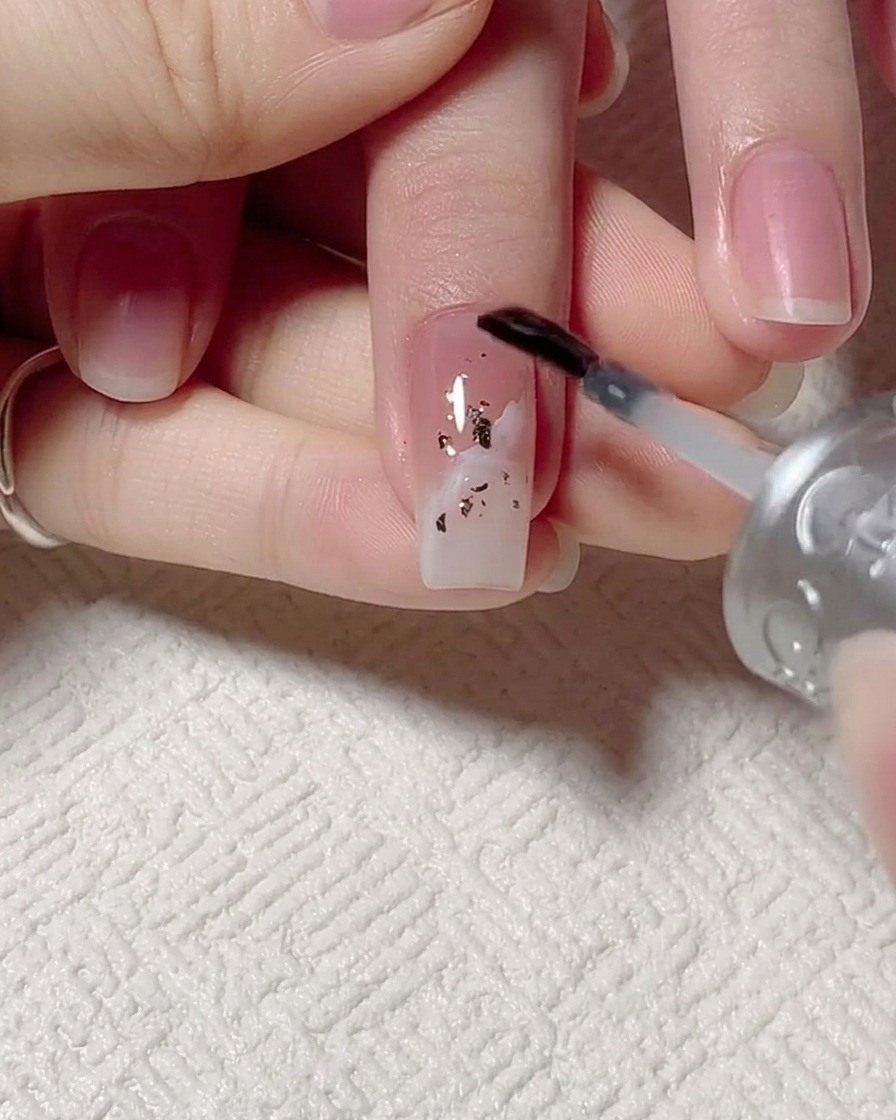 Ein Pinsel trägt klares Basisgel über das Design mit Blattgold und Wellen auf.